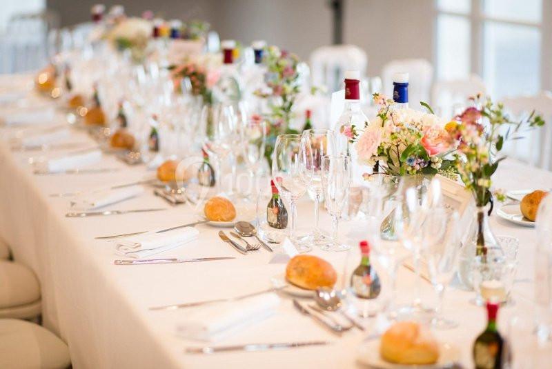 Table élégamment dressée avec nappes blanches, verres, couverts, fleurs et petits pains disposés pour un repas formel.