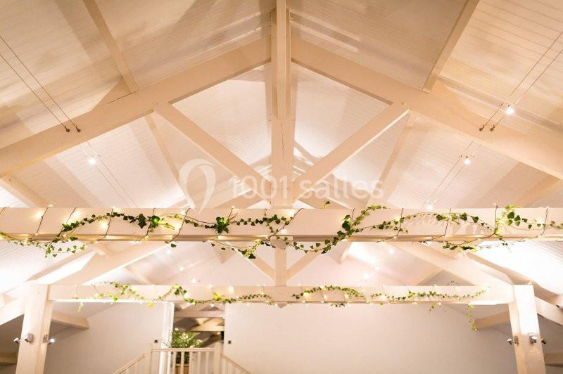 Plafond en bois peint en blanc avec des poutres apparentes décorées de guirlandes de feuillage et d'éclairages discrets.