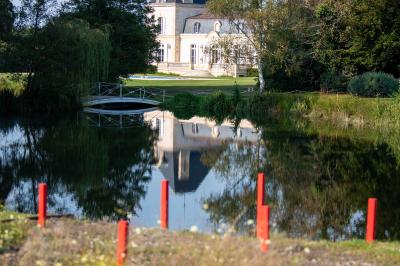 Miniature Location salle Léognan (Gironde) - Château Larrivet Haut-Brion #15 Manoir blanc entouré d'arbres, reflété dans un étang, avec des piquets rouges au premier plan.