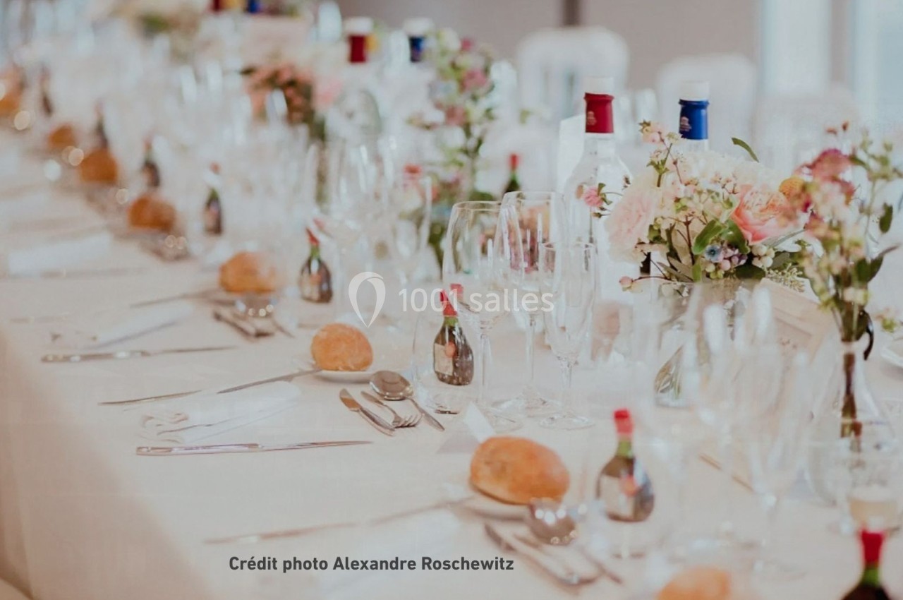 Table de réception élégamment dressée avec nappes blanches, verres, couverts, fleurs et bouteilles disposés harmonieusement.
