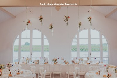 Table de réception élégamment dressée avec nappes blanches, verres, couverts, fleurs et bouteilles disposés harmonieusement.