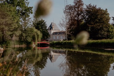 Vue sur une piscine extérieure entourée de pelouse, avec un lac et des arbres en arrière-plan sous un ciel dégagé.