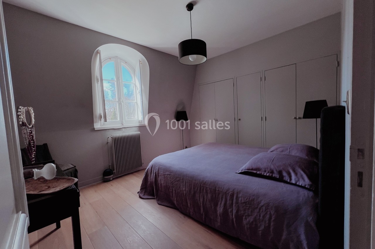 Chambre lumineuse avec un lit double, armoire encastrée, parquet en bois clair et une fenêtre cintrée.