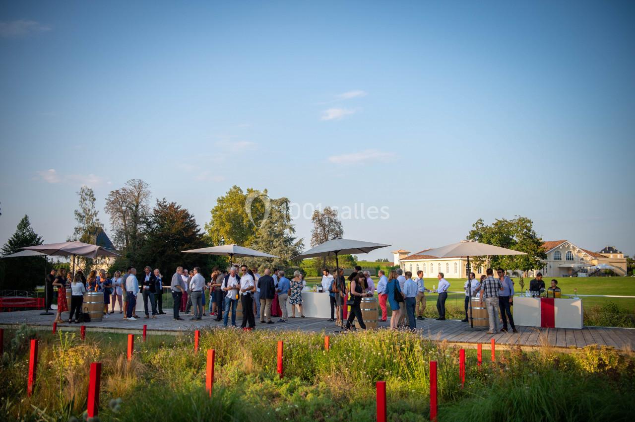Groupe de personnes rassemblées en extérieur autour de tables sous des parasols, dans un cadre verdoyant et ensoleillé.