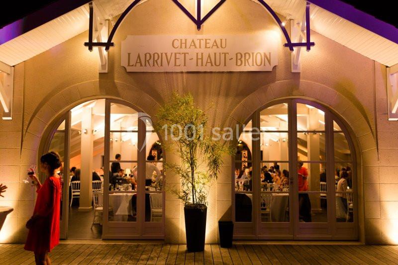Façade éclairée du Château Larrivet Haut-Brion avec des invités visibles à travers les grandes fenêtres.
