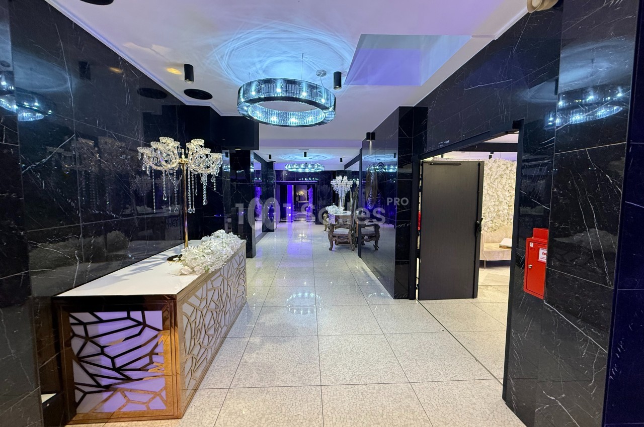Hall moderne avec murs noirs brillants, sol en carrelage clair, lustre lumineux et mobilier élégant.