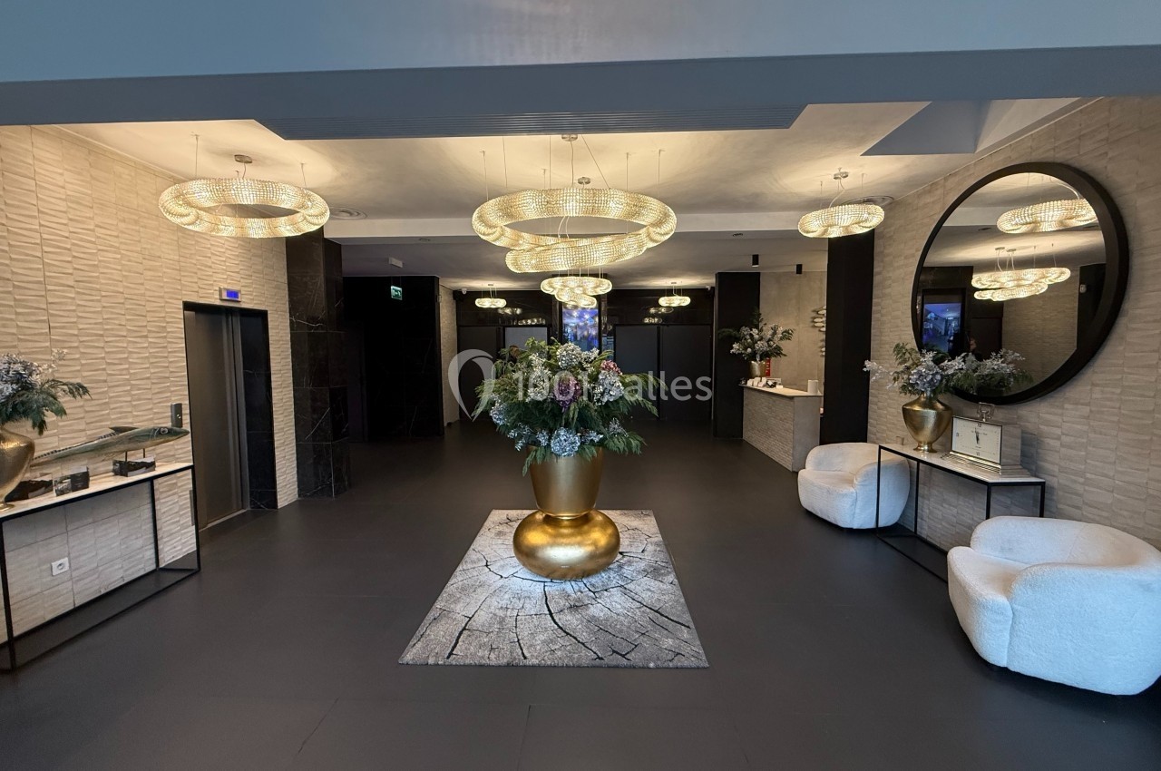 Hall d'entrée élégant avec un grand vase doré central, des lustres modernes et des fauteuils blancs.