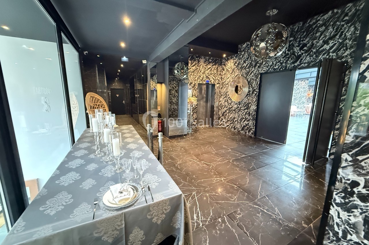 Salle moderne avec sol en marbre noir, table dressée à gauche et décorations murales métalliques réfléchissantes.