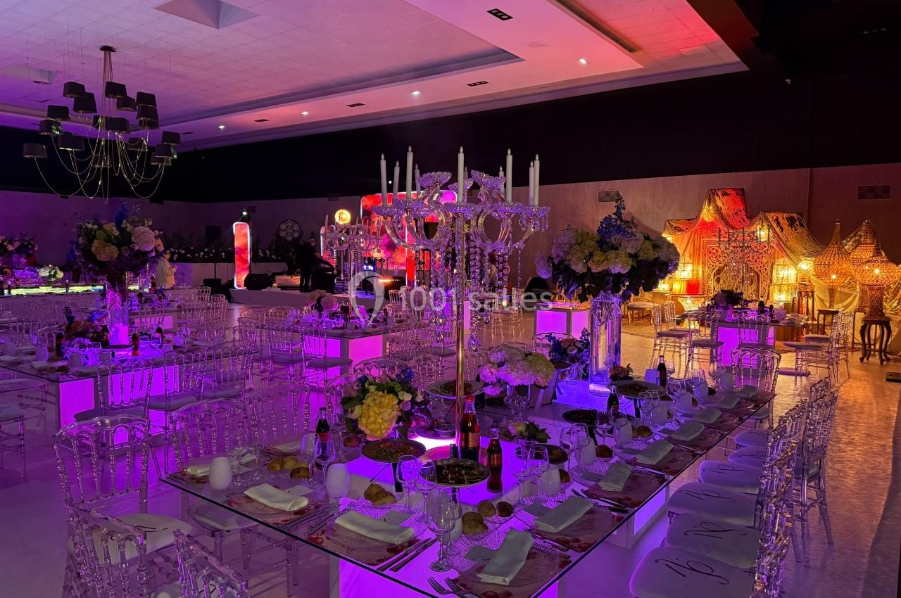 Salle de réception décorée avec des tables illuminées, chaises transparentes et éclairage coloré.