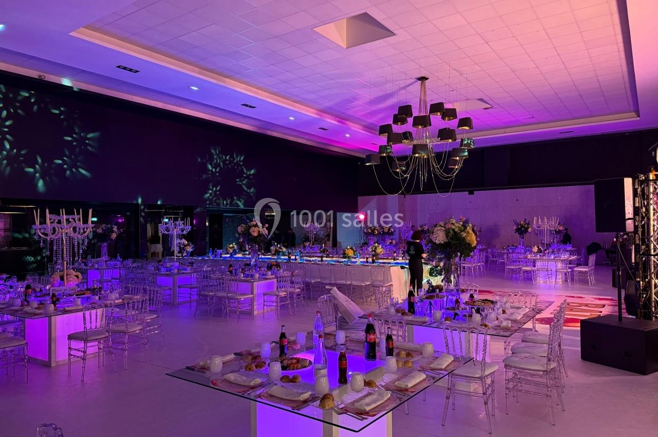 Salle de réception décorée avec des tables dressées, éclairage coloré et ambiance festive.