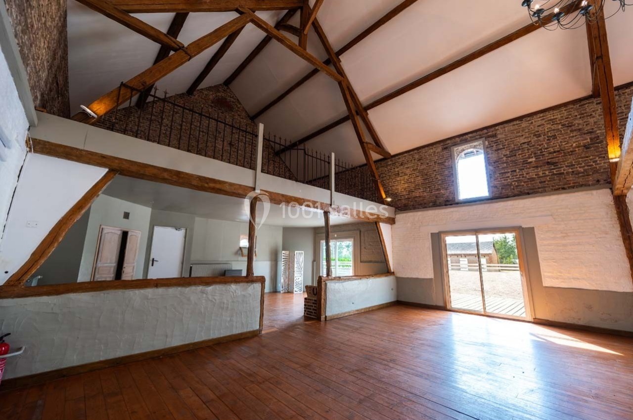 Intérieur d'une grande pièce lumineuse avec poutres apparentes, parquet en bois et mezzanine.