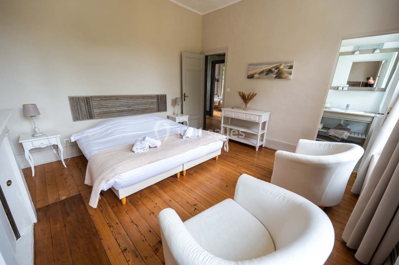 Chambre lumineuse avec lit double, mobilier blanc, parquet en bois et accès à une salle de bain attenante.
