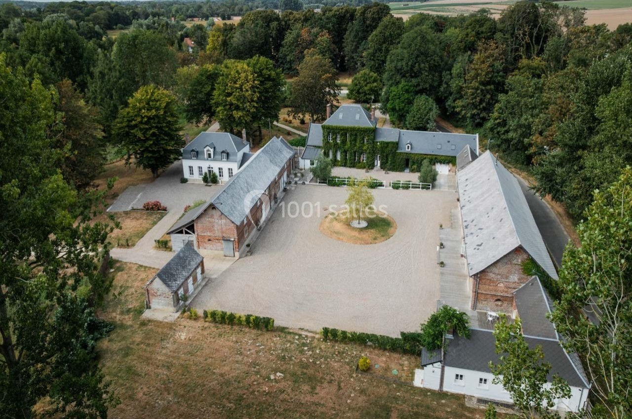 Vue aérienne d'une cour pavée entourée de bâtiments en briques et toits d'ardoise, au milieu d'un paysage arboré.