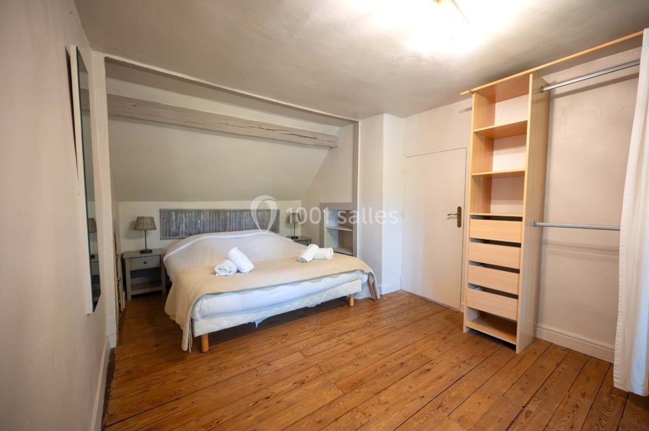 Chambre lumineuse avec lit double, parquet en bois, étagères ouvertes et murs clairs.