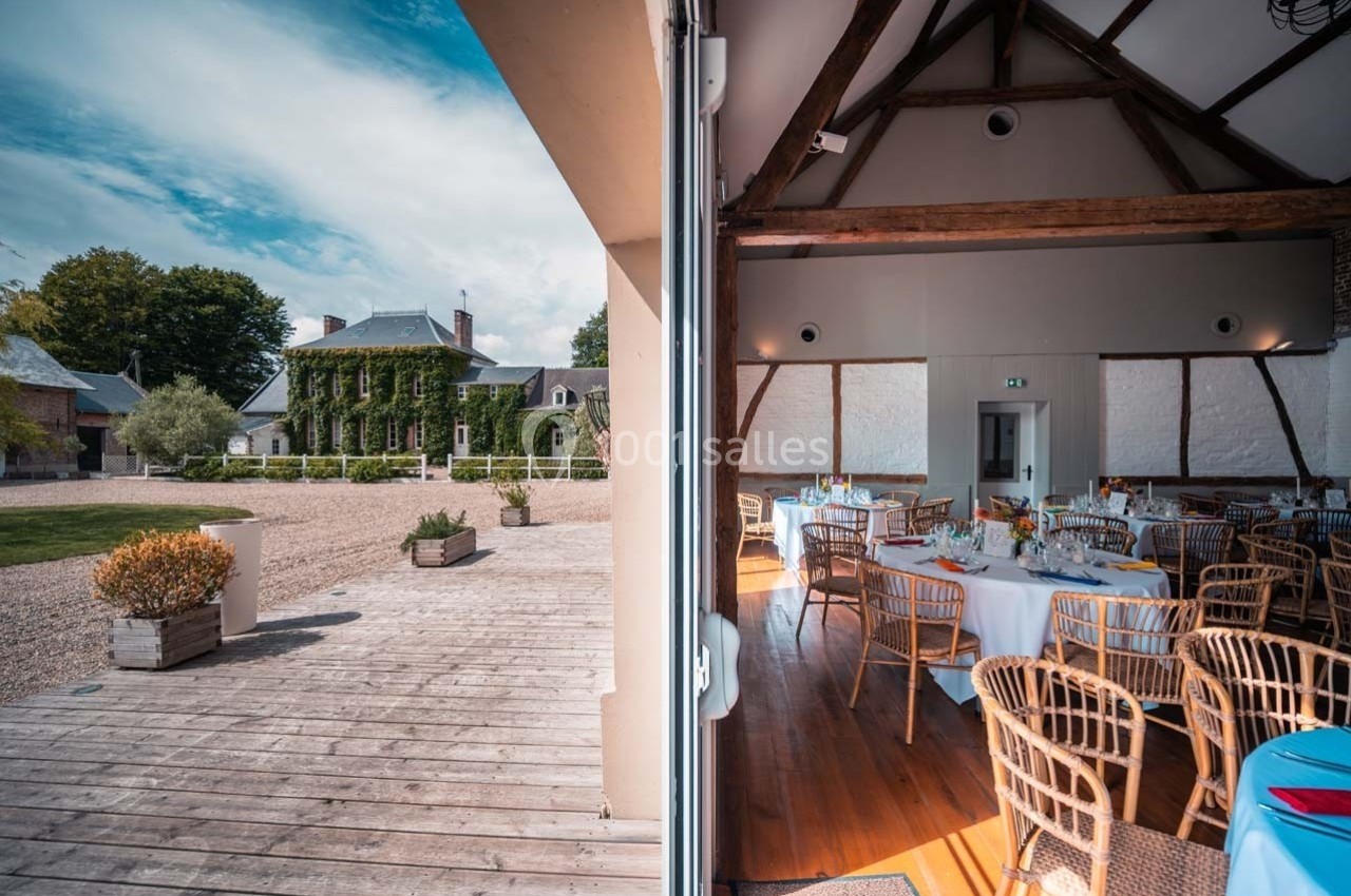 Vue d'un domaine avec une terrasse en bois et une salle de réception décorée, partiellement ouverte sur l'extérieur.