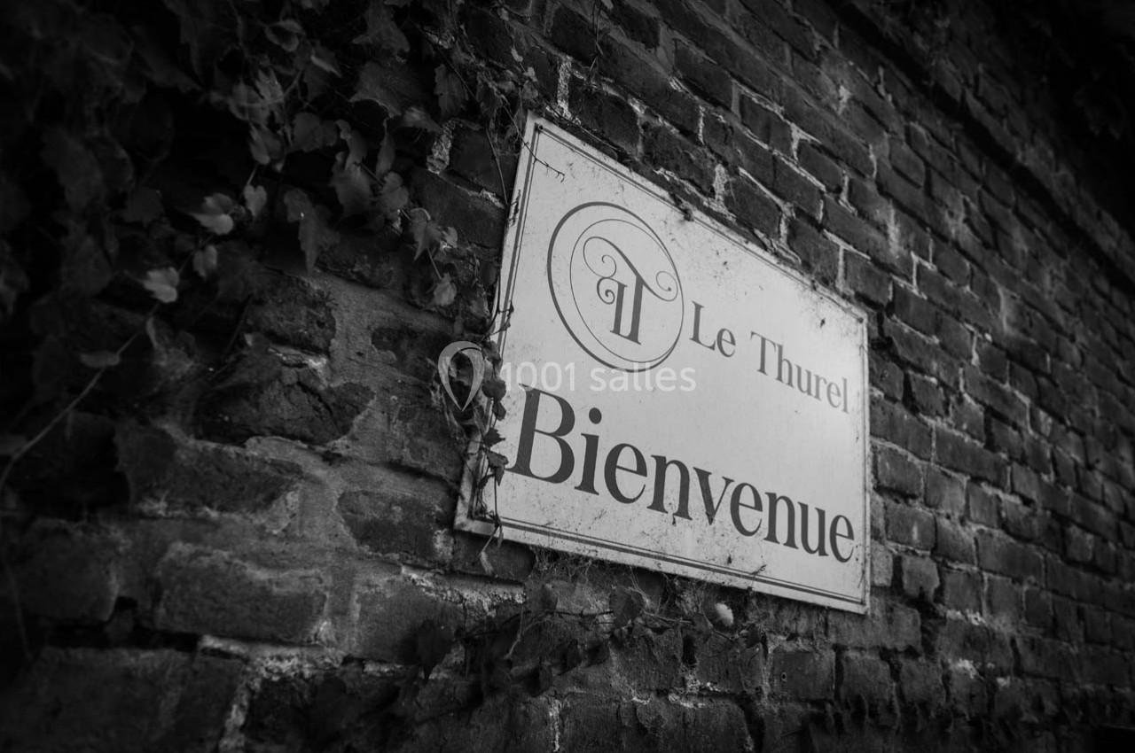Panneau ’Bienvenue’ fixé sur un mur de briques, entouré de quelques plantes grimpantes.
