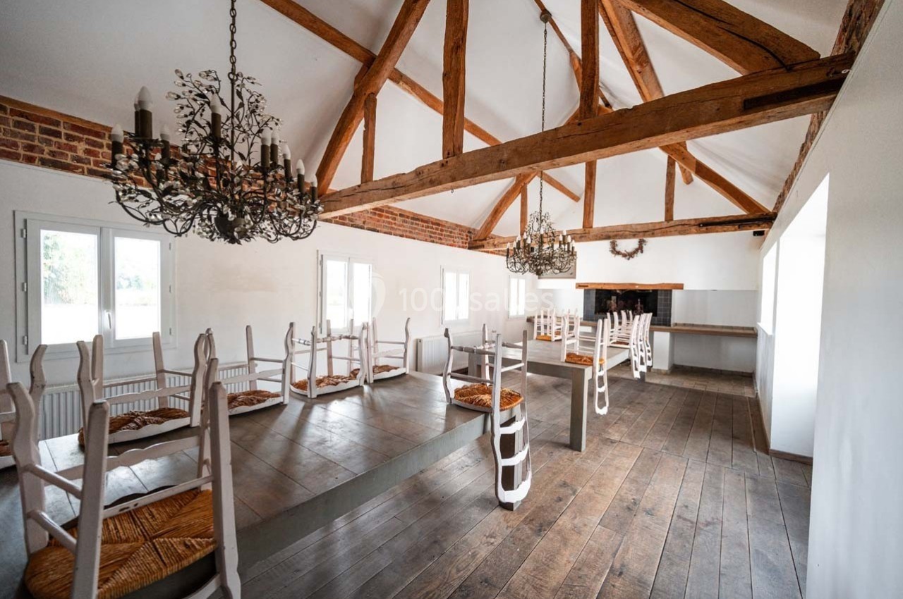 Salle lumineuse avec poutres apparentes, chaises retournées sur les tables en bois et lustres en fer forgé.