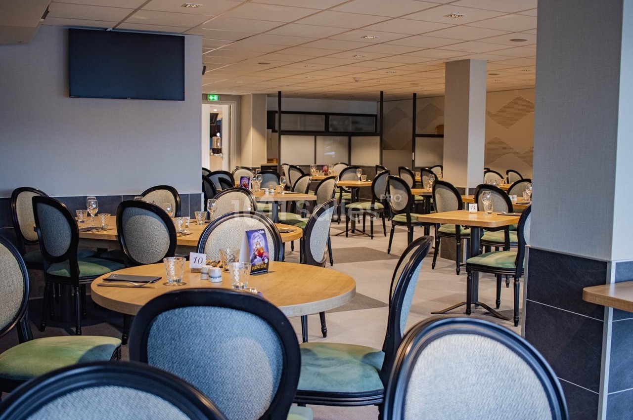 Salle de restaurant lumineuse avec des tables rondes dressées et des chaises rembourrées, décor sobre et moderne.