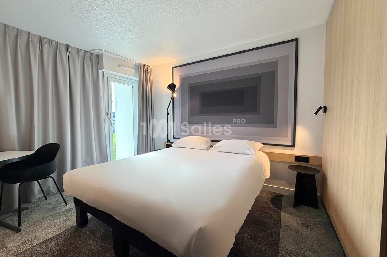 Chambre moderne avec un lit double, une grande œuvre murale abstraite, un bureau et des rideaux gris.