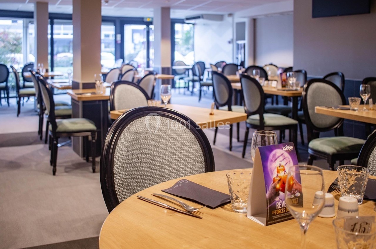 Salle de restaurant lumineuse avec des tables dressées, des chaises rembourrées et une vue sur l'extérieur.
