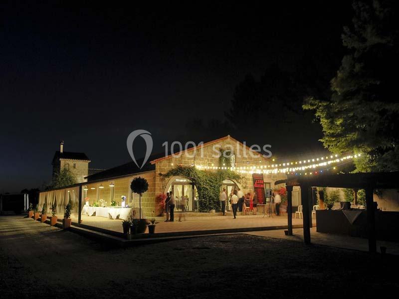 Bâtiment en pierre éclairé la nuit, décoré de guirlandes lumineuses, avec des tables dressées en extérieur.