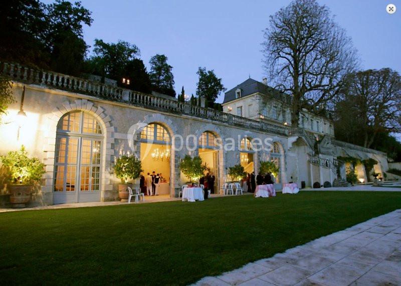 Façade éclairée d'un bâtiment historique avec grandes baies vitrées, entouré de verdure au crépuscule.