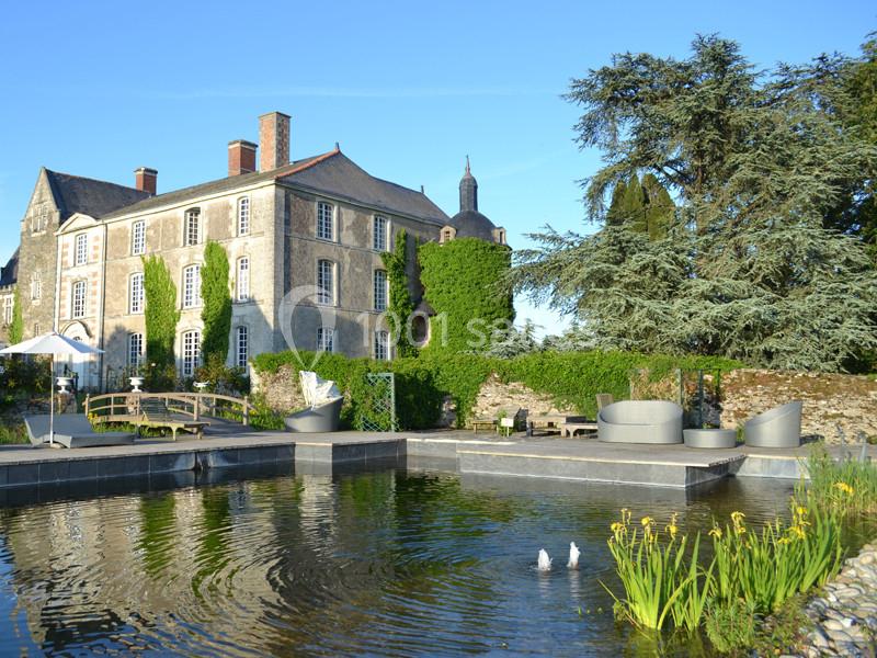 Manoir ancien entouré de verdure avec un bassin ornemental, des jets d'eau et des espaces de détente extérieurs.