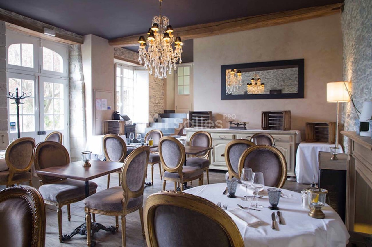 Salle de restaurant élégante avec chaises en bois sculpté, tables dressées et lustre en cristal suspendu.