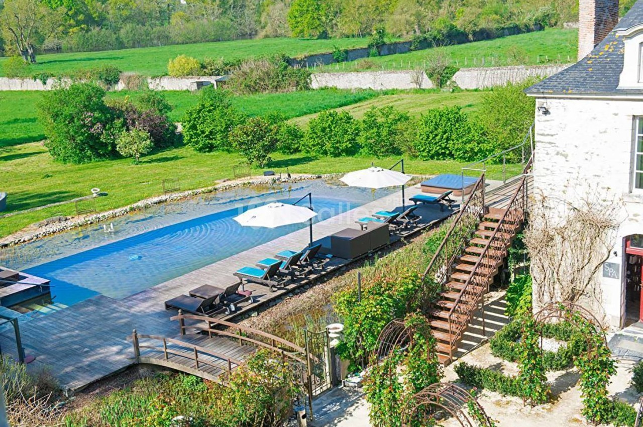 Piscine extérieure avec transats et parasols, entourée de verdure et située près d'une maison en pierre.