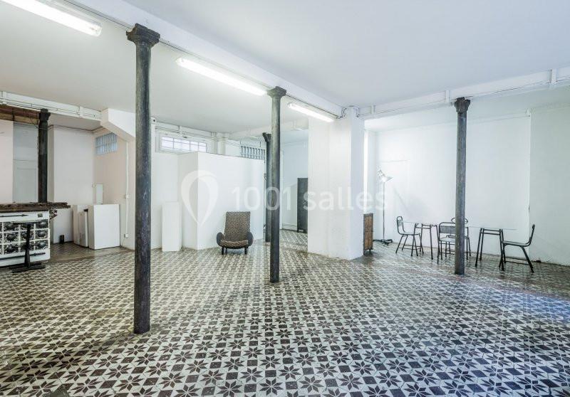Espace intérieur lumineux avec sol en carreaux de ciment, colonnes métalliques et mobilier minimaliste.