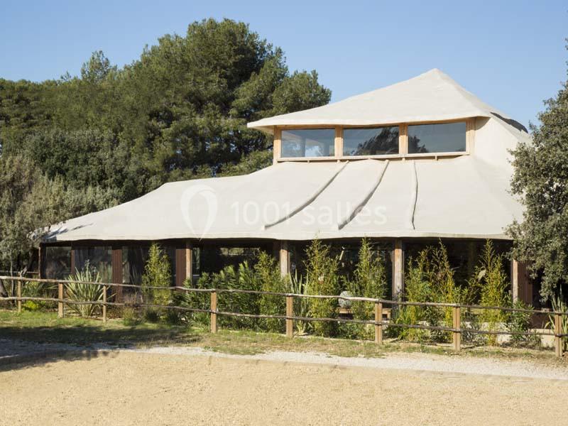 Bâtiment avec toit en toile beige, entouré de végétation et clôturé, situé dans un environnement naturel.