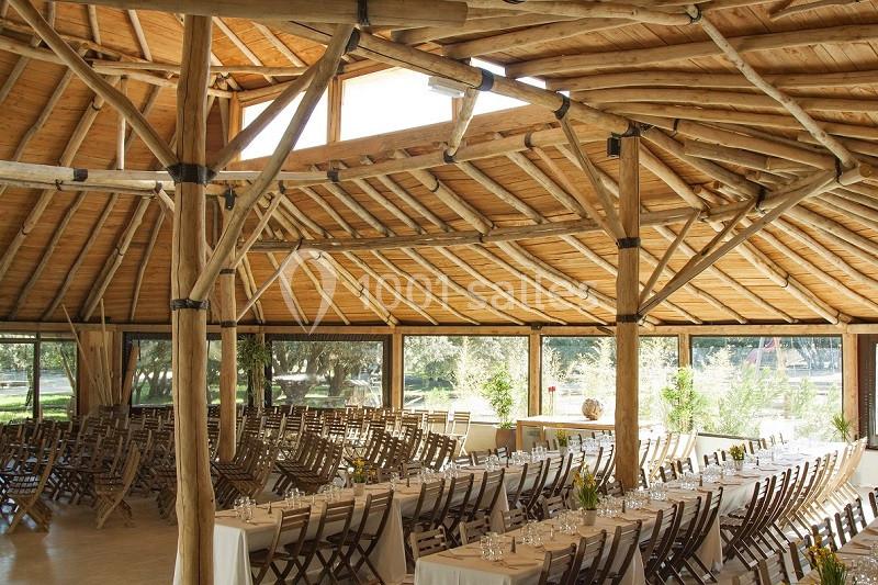 Salle circulaire en bois avec des tables dressées et des chaises alignées, éclairée par la lumière naturelle.