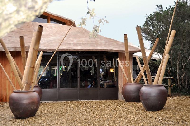 Entrée d'un bâtiment en bois avec de grandes jarres contenant des bambous, sur un sol en gravier.