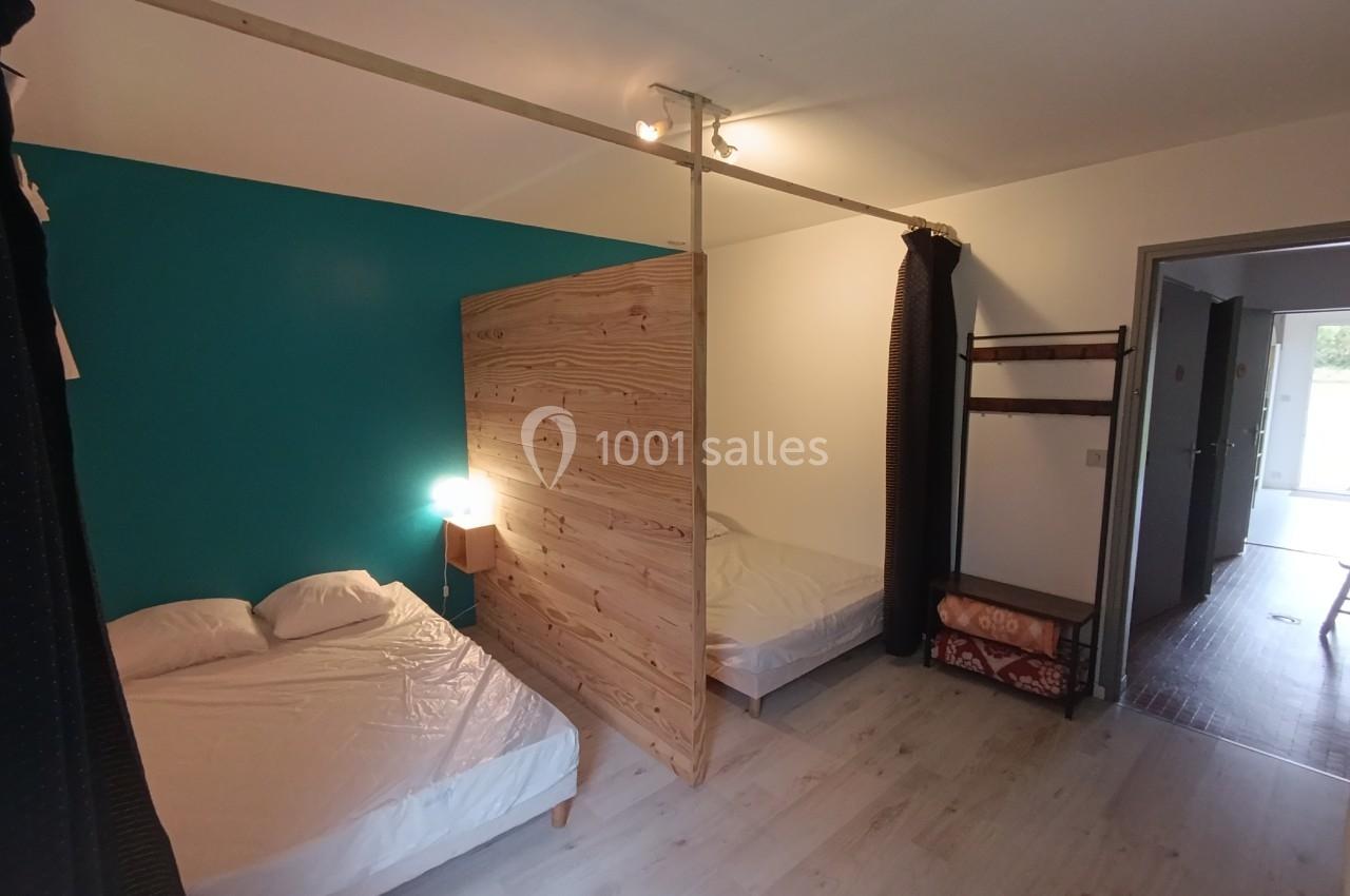 Chambre avec deux lits simples séparés par une cloison en bois, sol en parquet clair et mur peint en bleu.