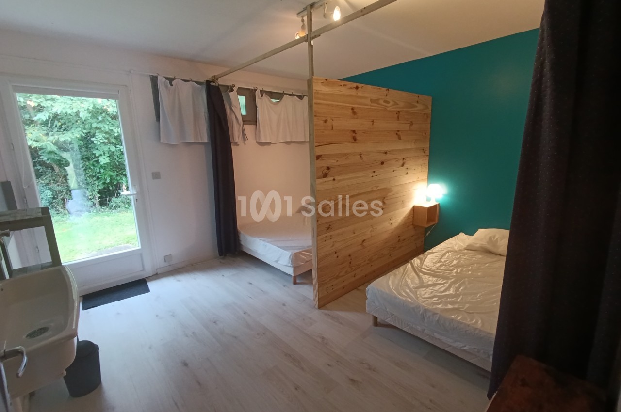 Chambre lumineuse avec deux lits séparés par une cloison en bois, vue sur un jardin par une porte vitrée.