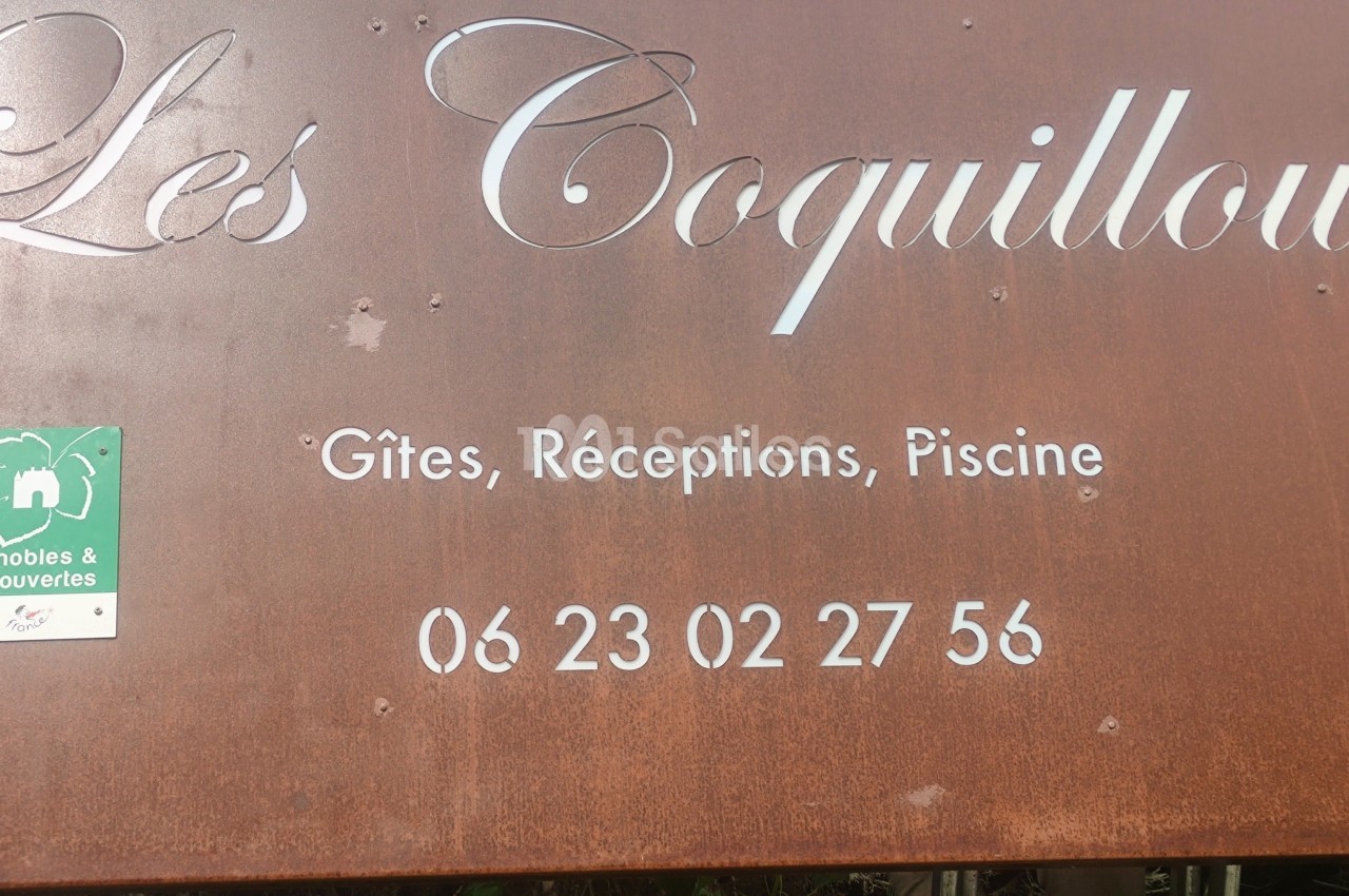 Panneau en métal rouillé indiquant ’Les Coquilloux’, avec des informations sur des gîtes, réceptions, piscine et un numéro…