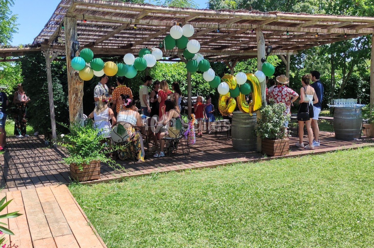 Personnes rassemblées sous une pergola décorée de ballons colorés dans un jardin verdoyant.