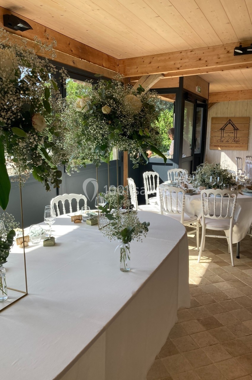 Salle de réception lumineuse avec tables décorées de nappes blanches, chaises élégantes et arrangements floraux.