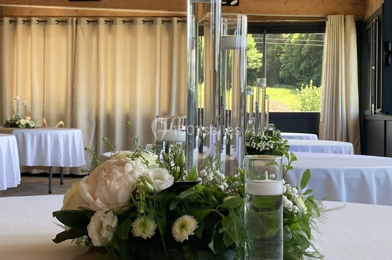 Centre de table floral avec bougies flottantes dans une salle lumineuse décorée pour un événement.