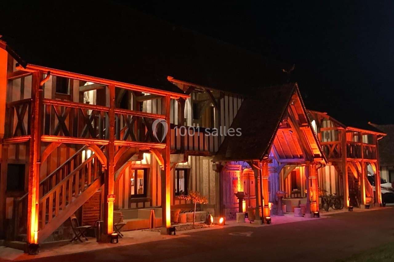 Façade d'un bâtiment à colombages éclairée par des lumières orange et rouges dans un environnement nocturne.