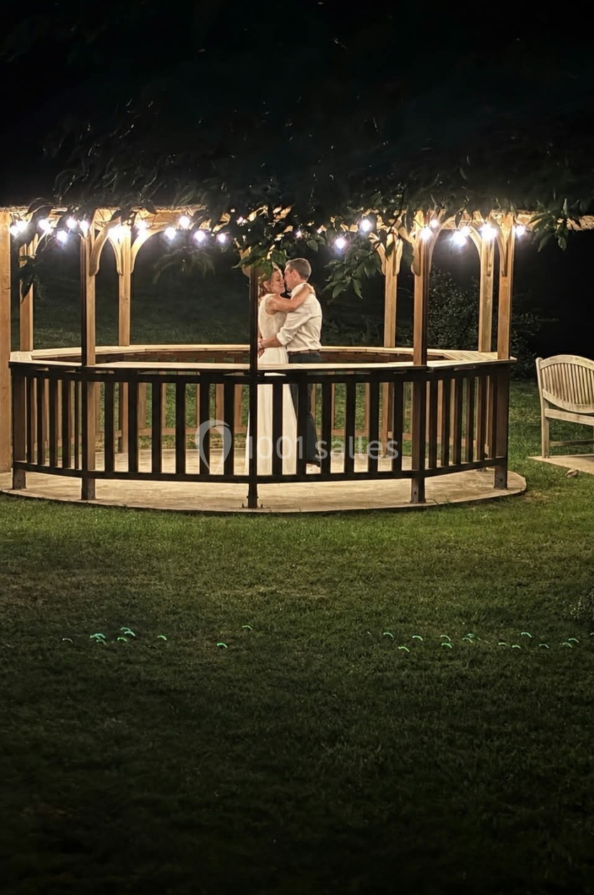 Un couple danse sous un kiosque en bois éclairé, entouré d'herbe et d'obscurité nocturne.