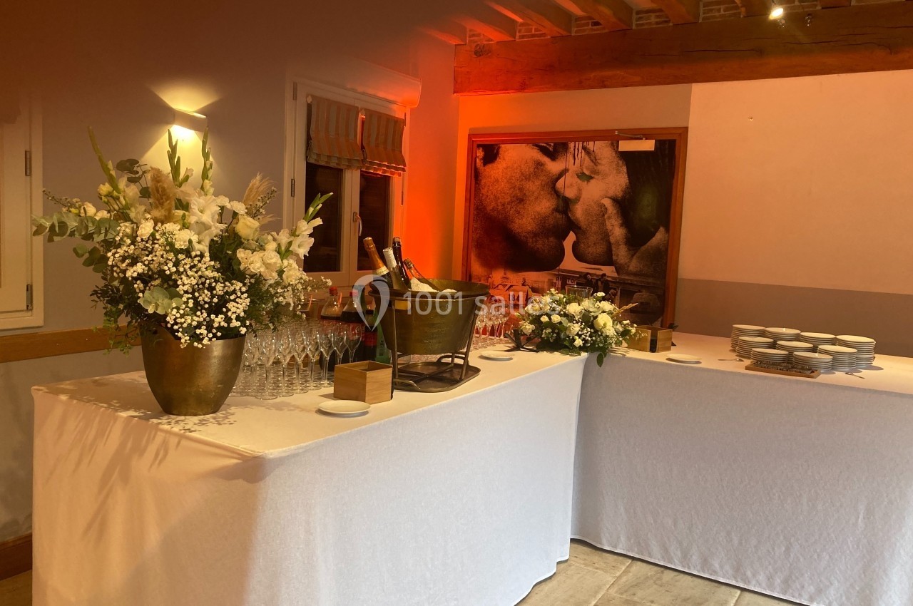 Table dressée avec nappes blanches, fleurs, seau à champagne, verres et assiettes dans une salle éclairée chaleureusement.