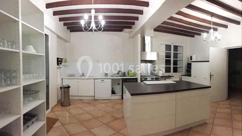 Cuisine spacieuse avec îlot central, poutres apparentes, étagères ouvertes et électroménagers modernes.