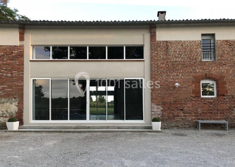Façade d'un bâtiment en briques avec une grande baie vitrée et des pots de fleurs blancs de chaque côté.