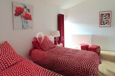 Deux lits simples avec housses rouges à pois blancs dans une chambre lumineuse décorée de touches rouges et blanches.
