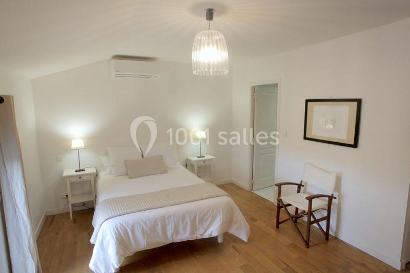 Chambre lumineuse avec lit double, parquet en bois, deux tables de chevet, une chaise et un éclairage suspendu.