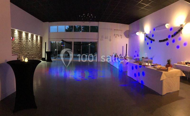 Salle de réception décorée avec des guirlandes, tables de buffet dressées et éclairage tamisé bleu.