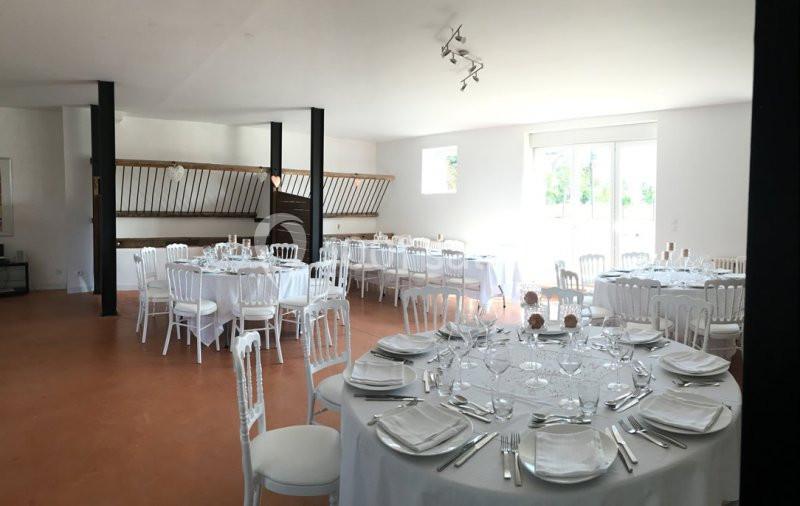 Salle lumineuse avec tables rondes dressées pour un repas, chaises blanches et sol en terre cuite.