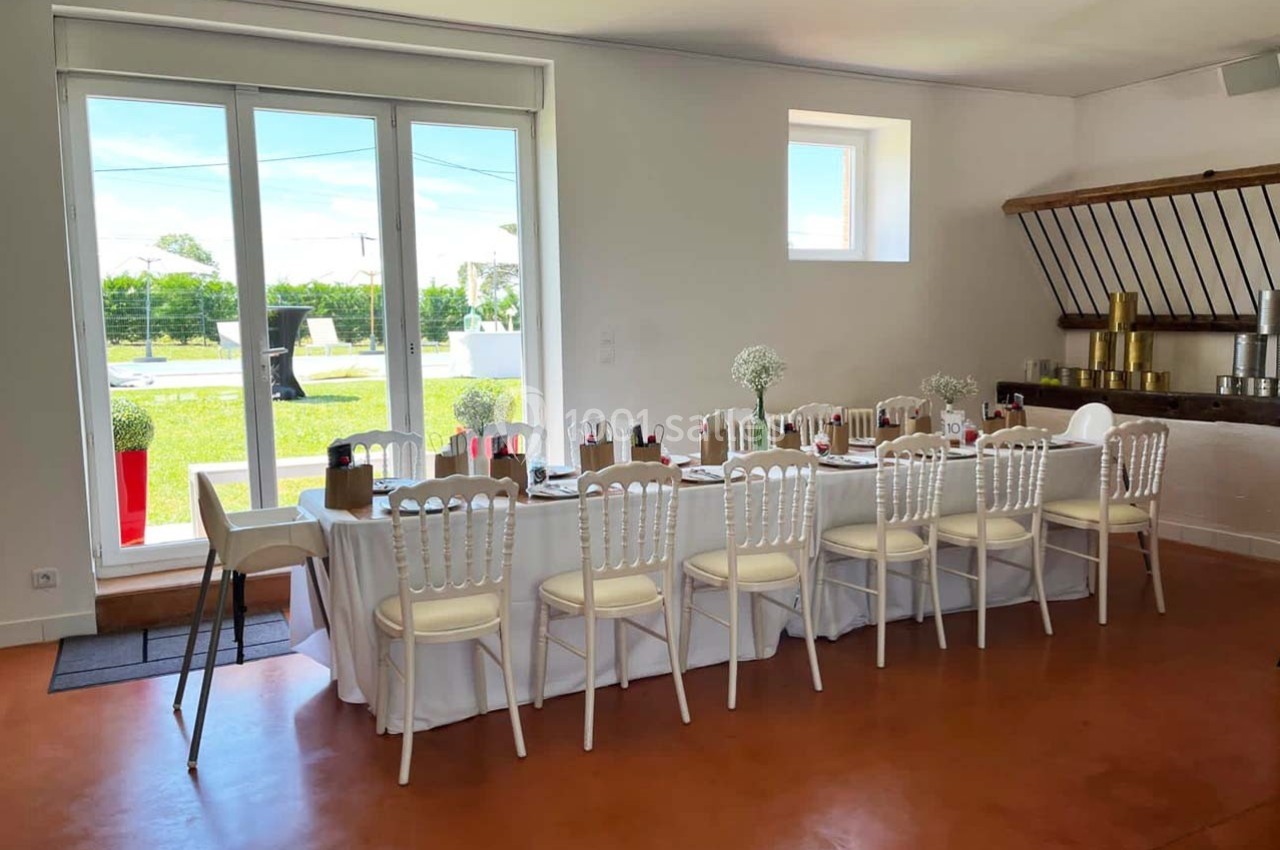 Location salle Sainte-Foy-d'Aigrefeuille (Haute-Garonne) - Les Ecuries de Ronsac #4 Salle lumineuse avec une grande table dressée pour un repas, chaises blanches et vue sur un jardin à travers une baie vitrée.