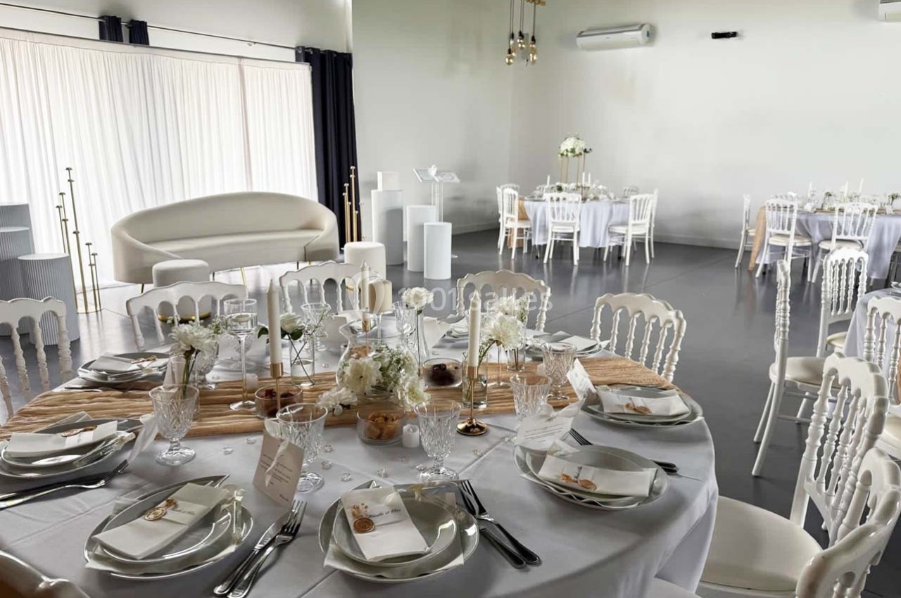 Location salle Sainte-Foy-d'Aigrefeuille (Haute-Garonne) - Les Ecuries de Ronsac #5 Salle de réception lumineuse avec tables rondes dressées, nappes blanches, décorations florales et chaises élégantes.